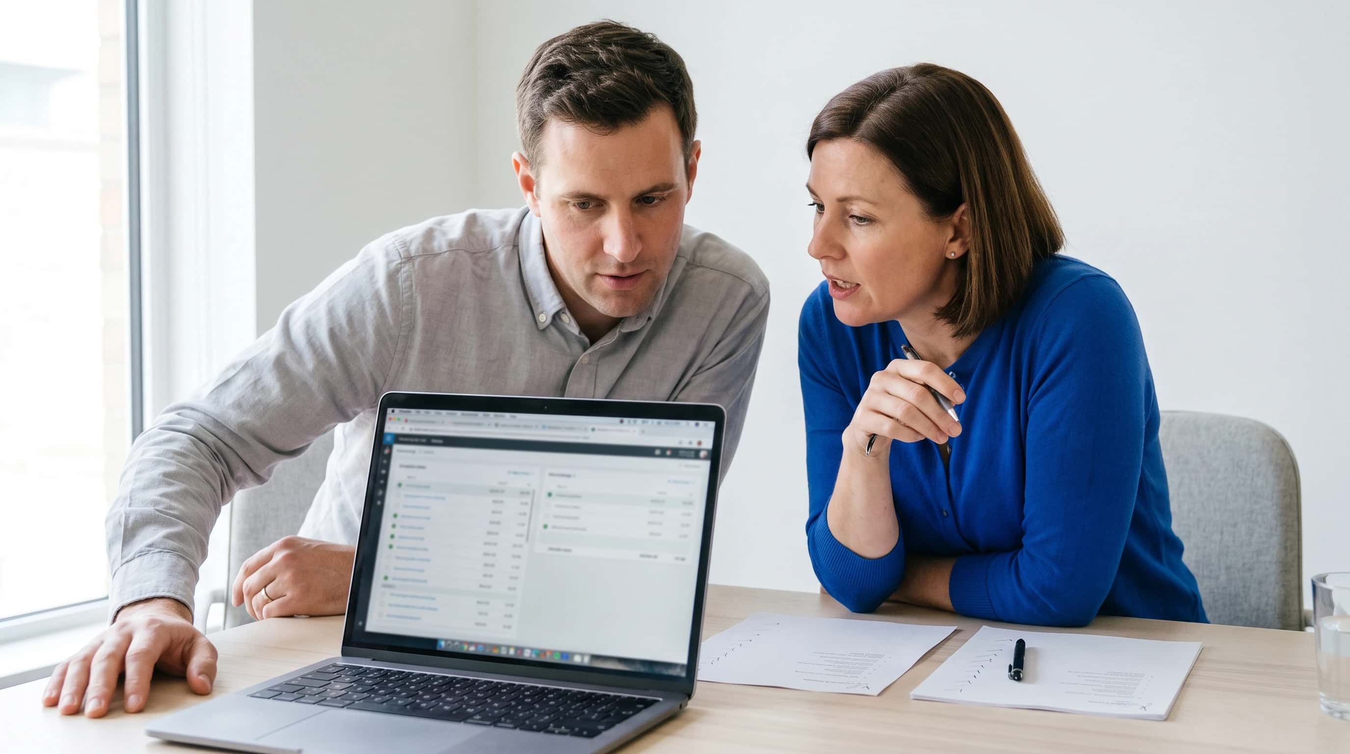 Twee collega-ontwikkelaars kijken samen naar een laptopscherm met een reconciliatie-overzicht, in een licht kantoor met blauw accent