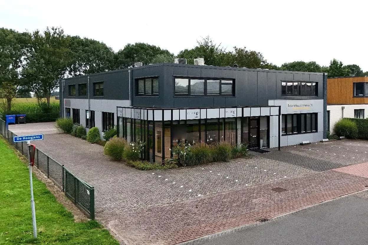 Gevel van het kantoor aan De Hoogjens 1a in Sleeuwijk, met de glazen hoekpartij en de parkeerplaats