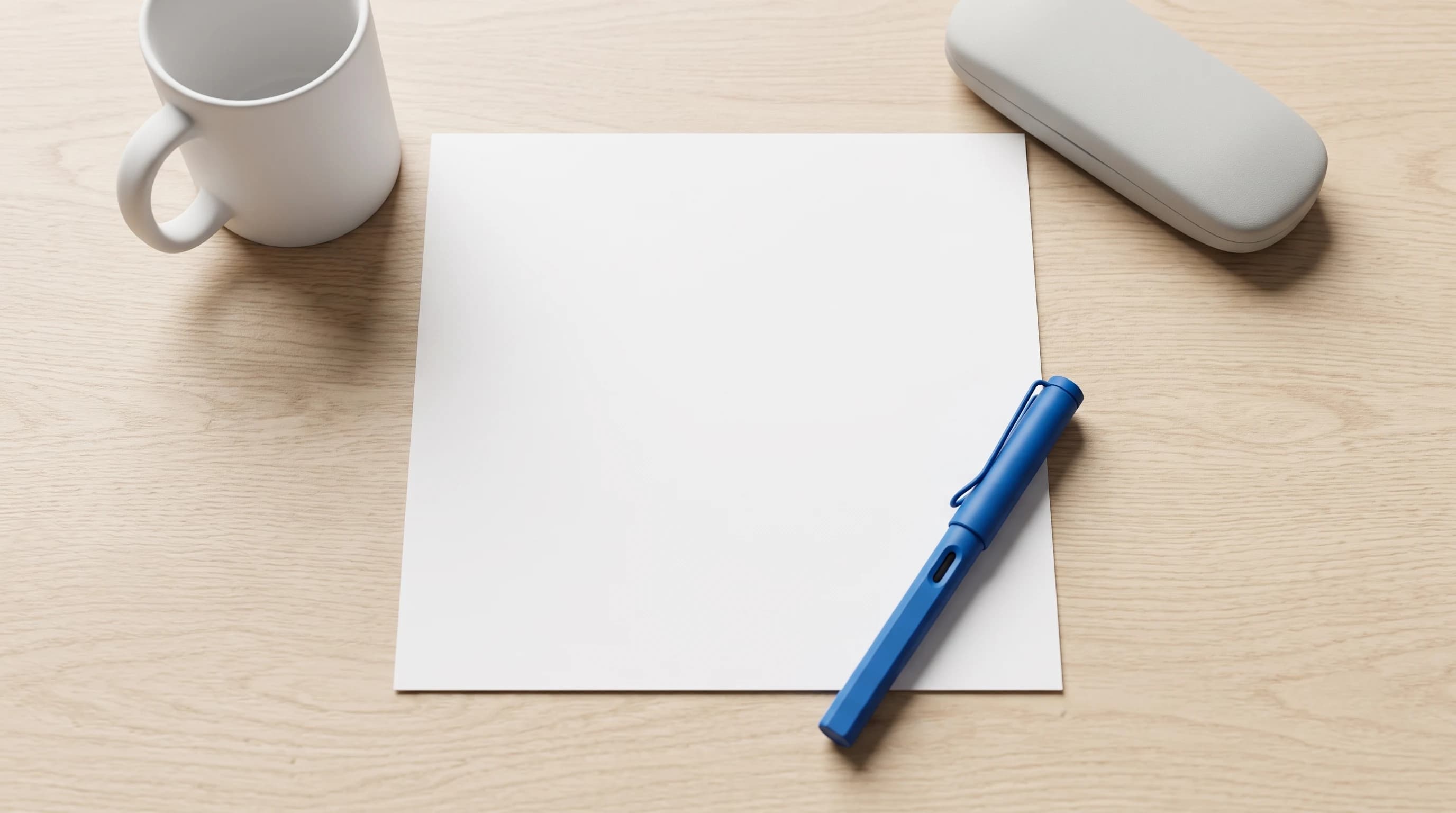 Eén blanco A4 op een licht eiken bureau met een blauwe vulpen, een witte mok en een brillenkoker