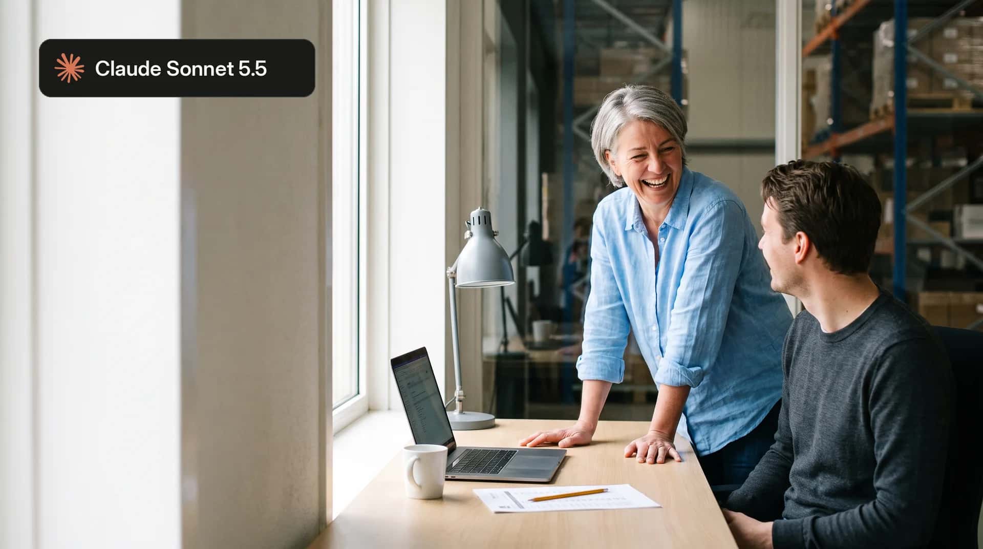 Lachende vrouw bij een bureau met een collega achter een laptop in een magazijnkantoor, met het label Claude Sonnet 5.5