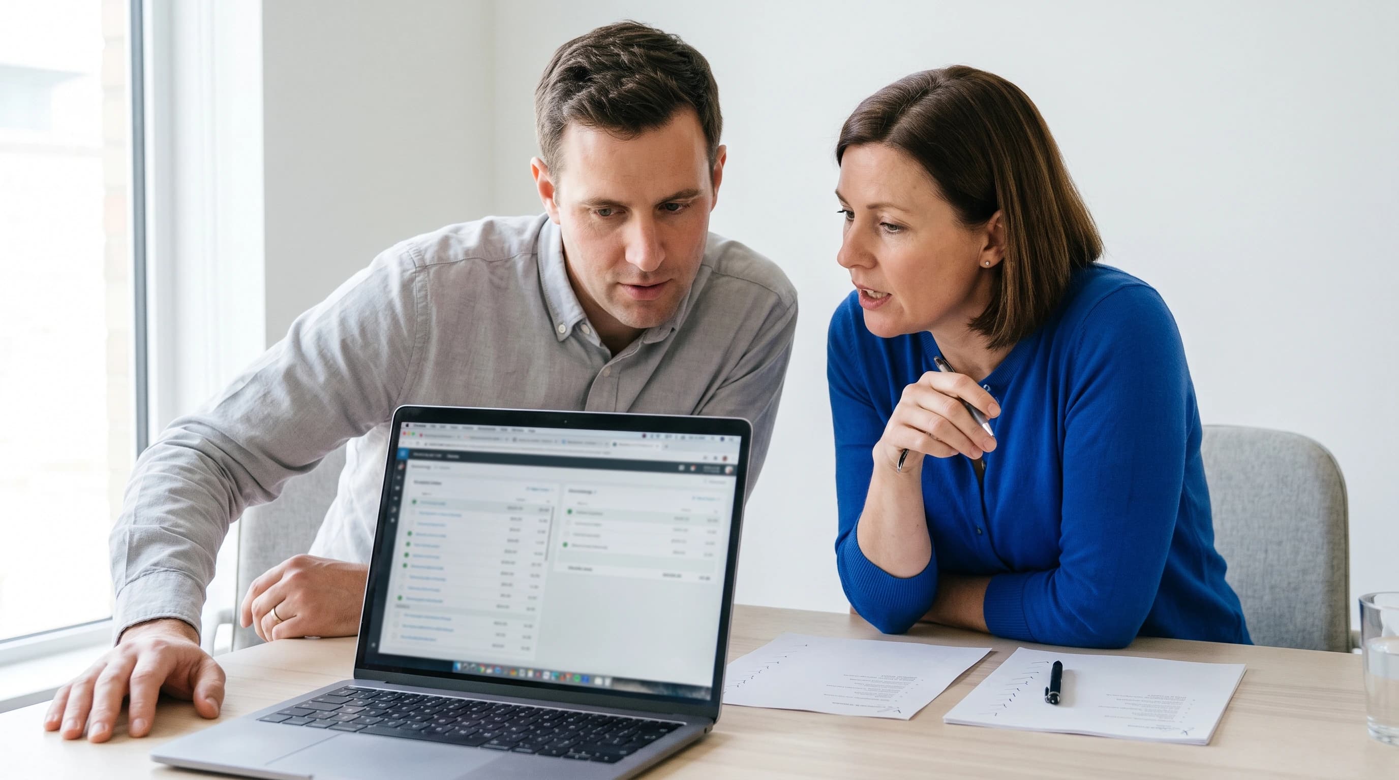 Twee collega-ontwikkelaars kijken samen naar een laptopscherm met een reconciliatie-overzicht, in een licht kantoor met blauw accent