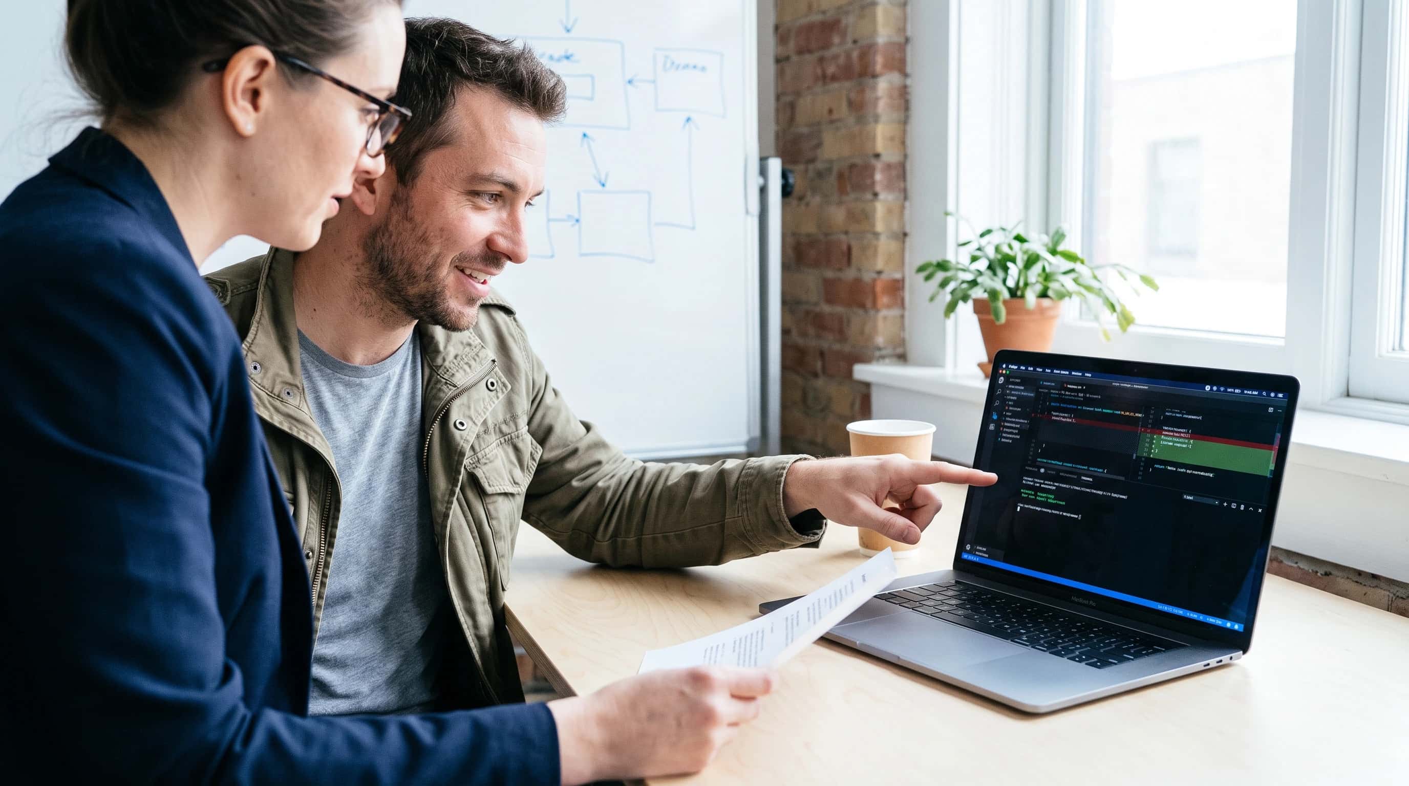 Ontwikkelaar en opdrachtgever kijken samen naar een codewijziging en testresultaten op een laptop tijdens een reviewmoment