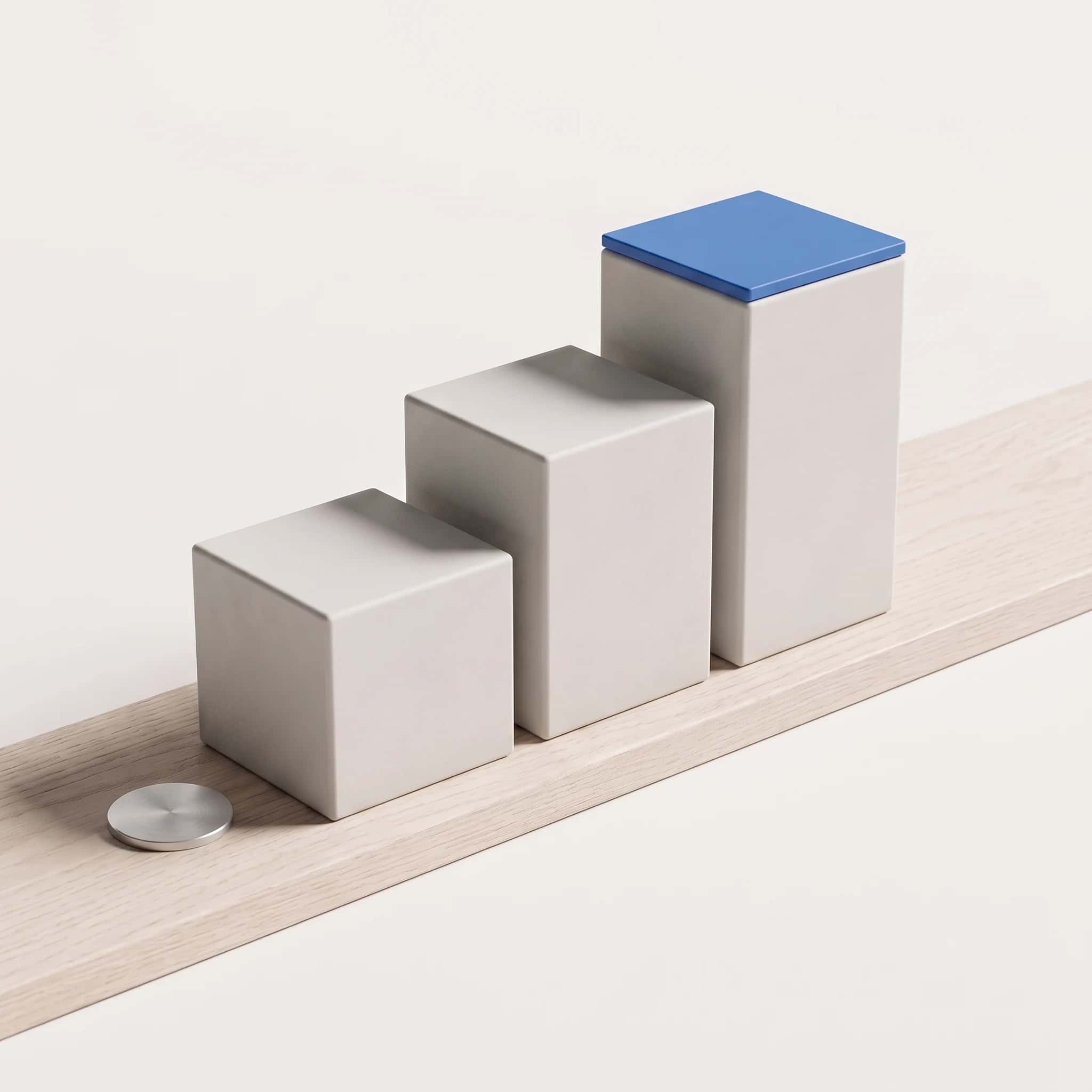 Drie lichtgrijze matte blokken van oplopende hoogte op een licht eiken plank, het hoogste blok met een blauwe dekplaat