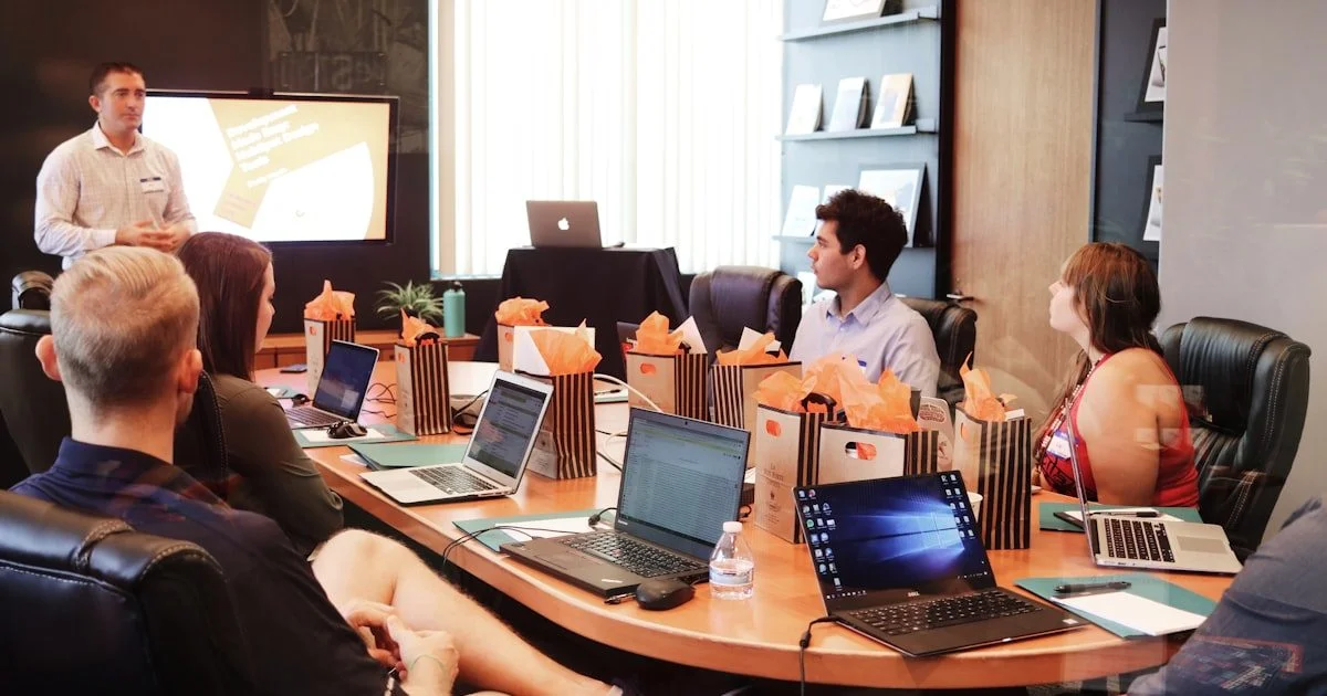 Trainer geeft presentatie aan team met laptops in vergaderruimte, symbool voor verplichte AI-geletterdheid en digitale educatie op de werkvloer