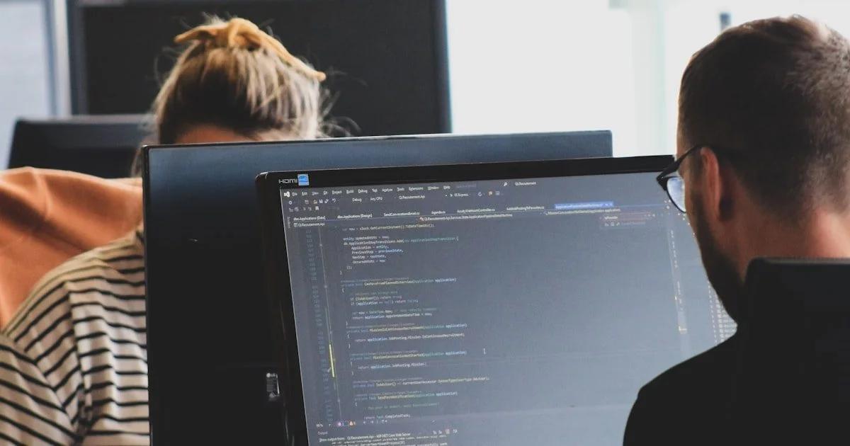 Persoon in hoodie die code typt op een computerscherm als beeld voor security auditing en penetratietesten van AI-systemen