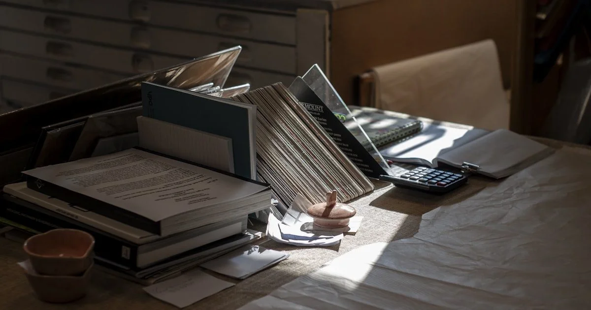 Rommelig bureau met papieren, boeken en calculator - symbool voor verborgen kosten van handmatig administratief werk