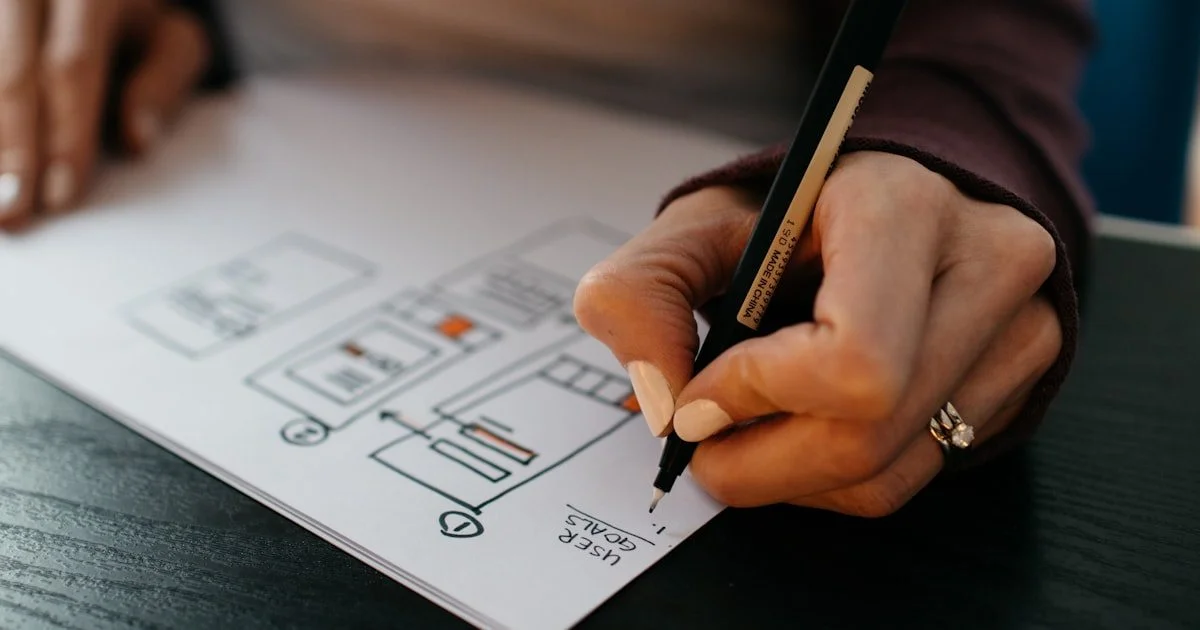 Designer schetst wireframe op papier met pen — voorbereidingsfase van website redesign en UX-verbetering
